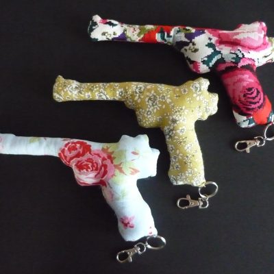 hree flower patterned fabric guns sit on a black background. All three guns have a key chain hanging from the base.